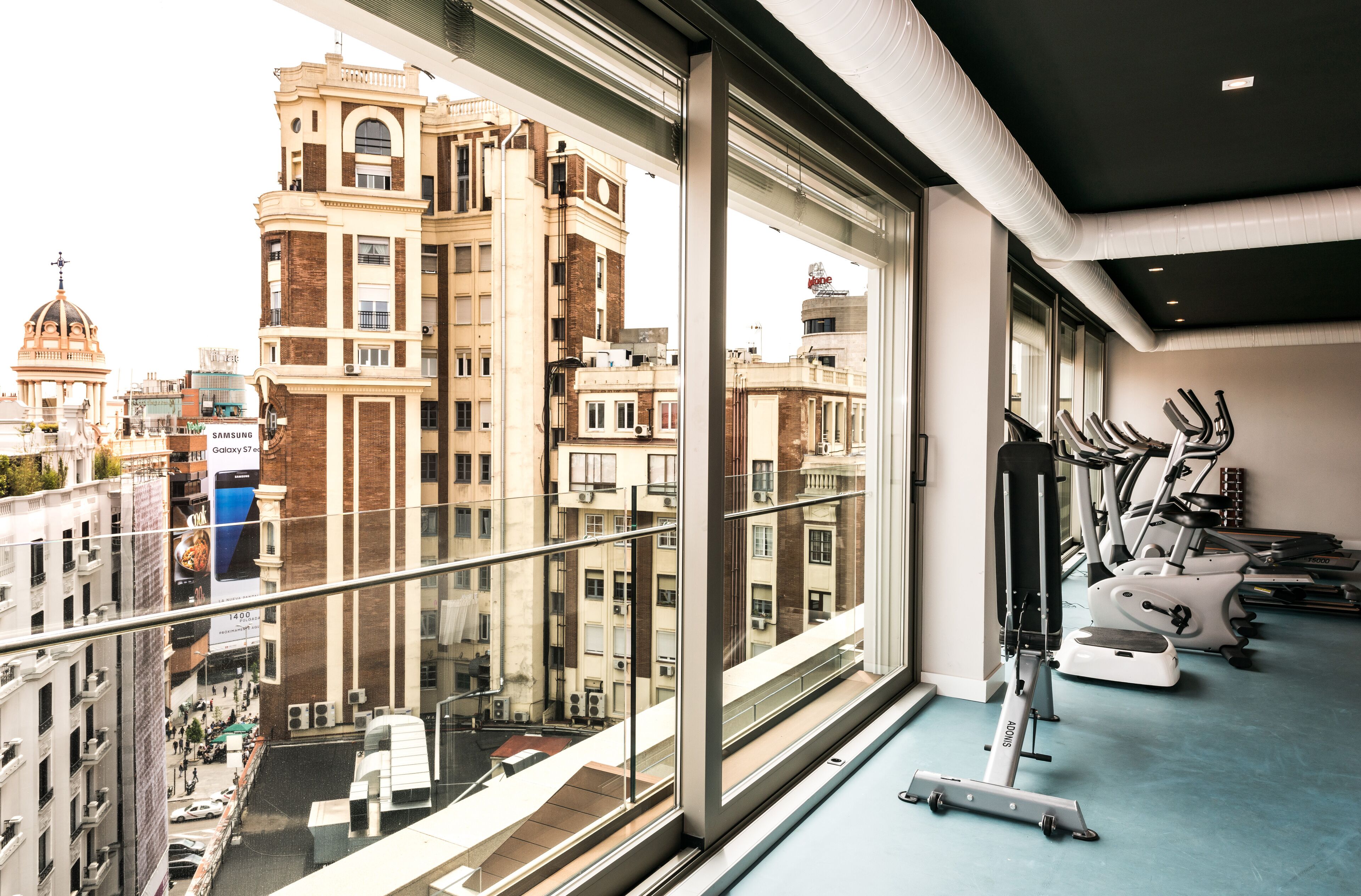 A gym with exercise equipment and a view of city buildings through large windows.