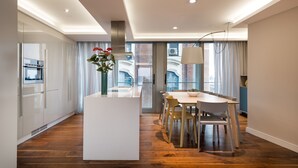 A modern kitchen with a central island, wooden flooring, and a dining area with chairs and a table. - Gran View Apartments (Madrid)