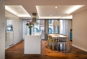 A modern kitchen with a central island, wooden flooring, and a dining area with chairs and a table.