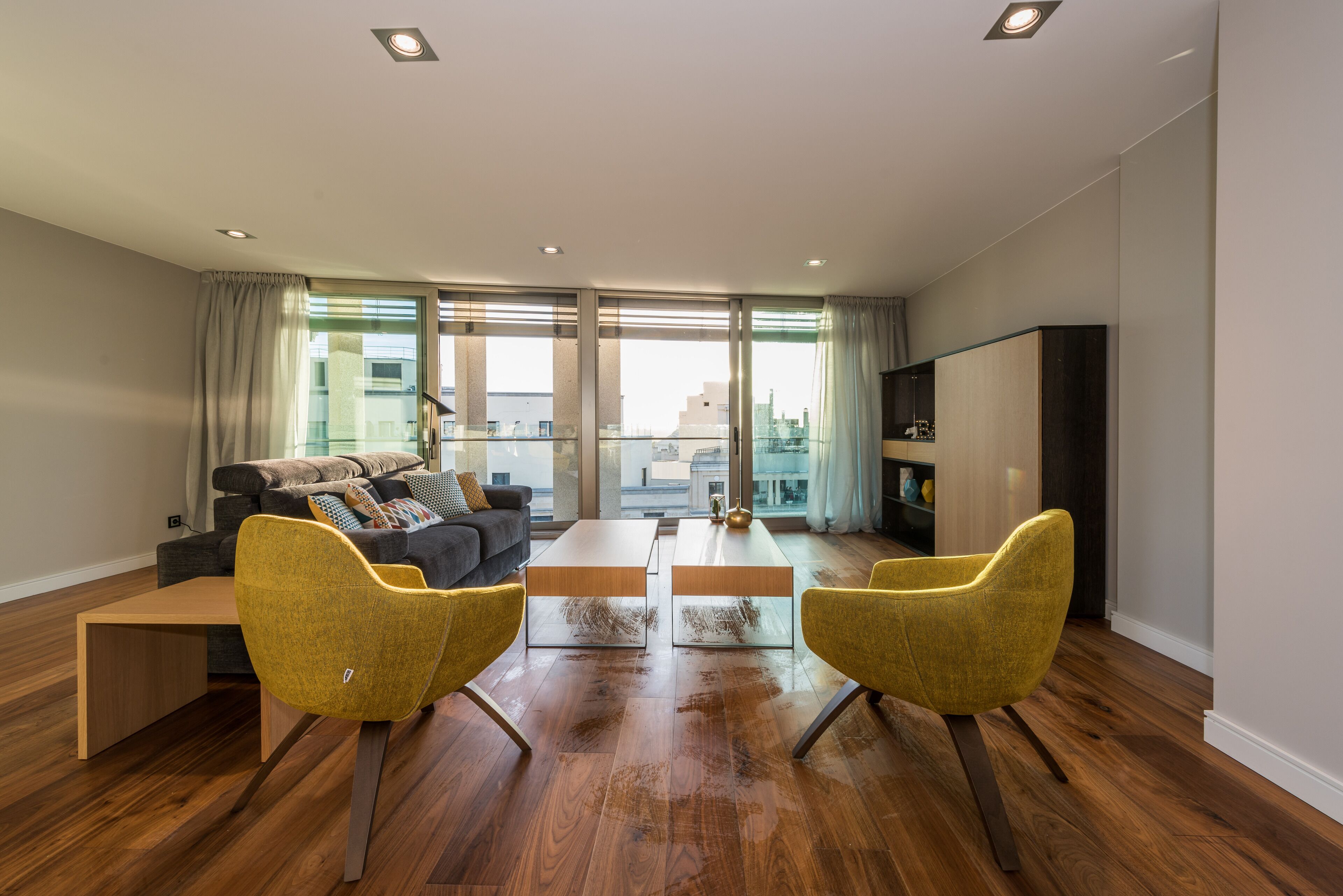 Una sala de estar moderna con un sofá, dos sillones amarillos, una mesa de centro y un mueble para televisor.