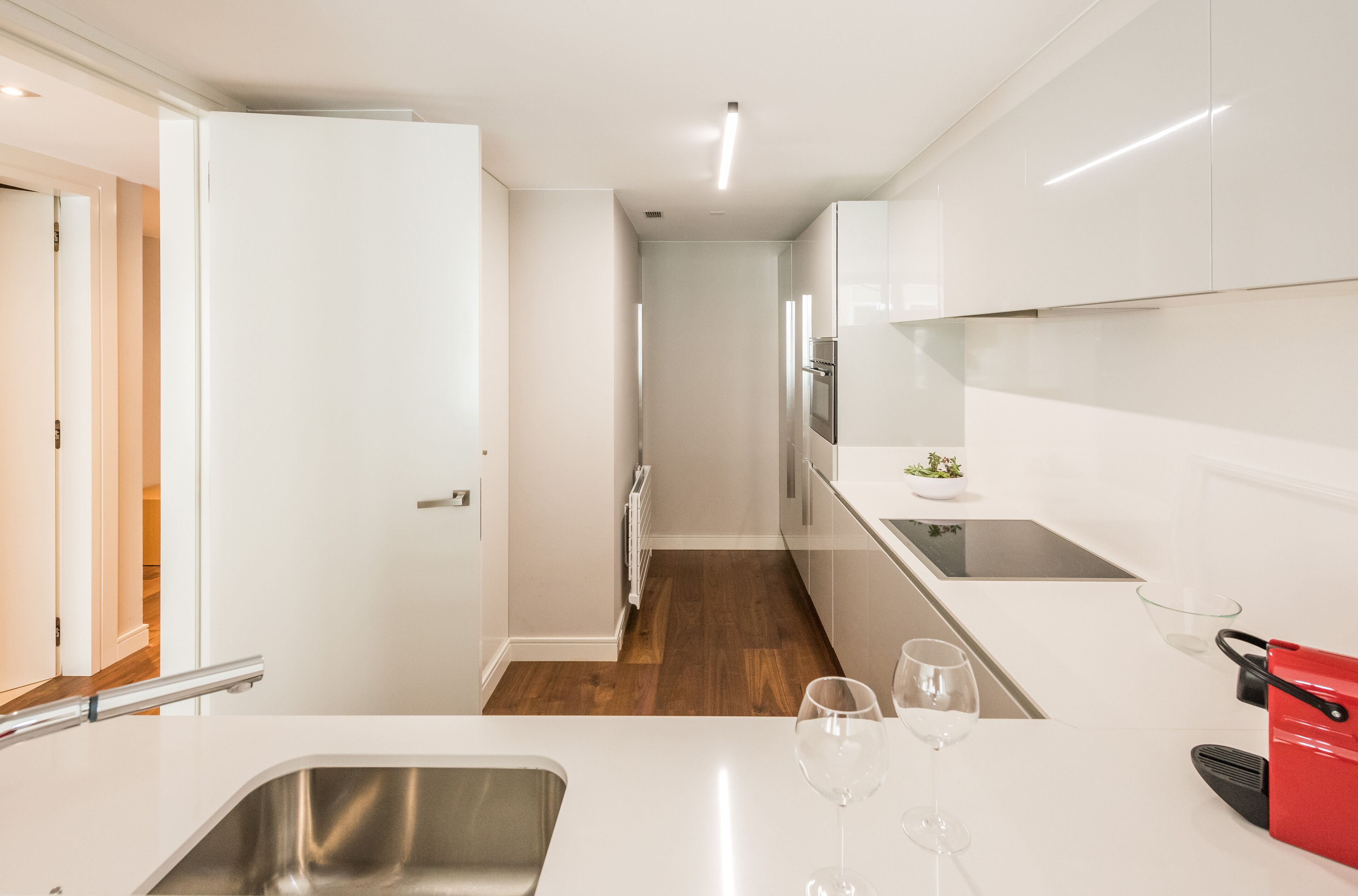 A modern kitchen with white cabinets, a stainless steel sink, and a red kettle.