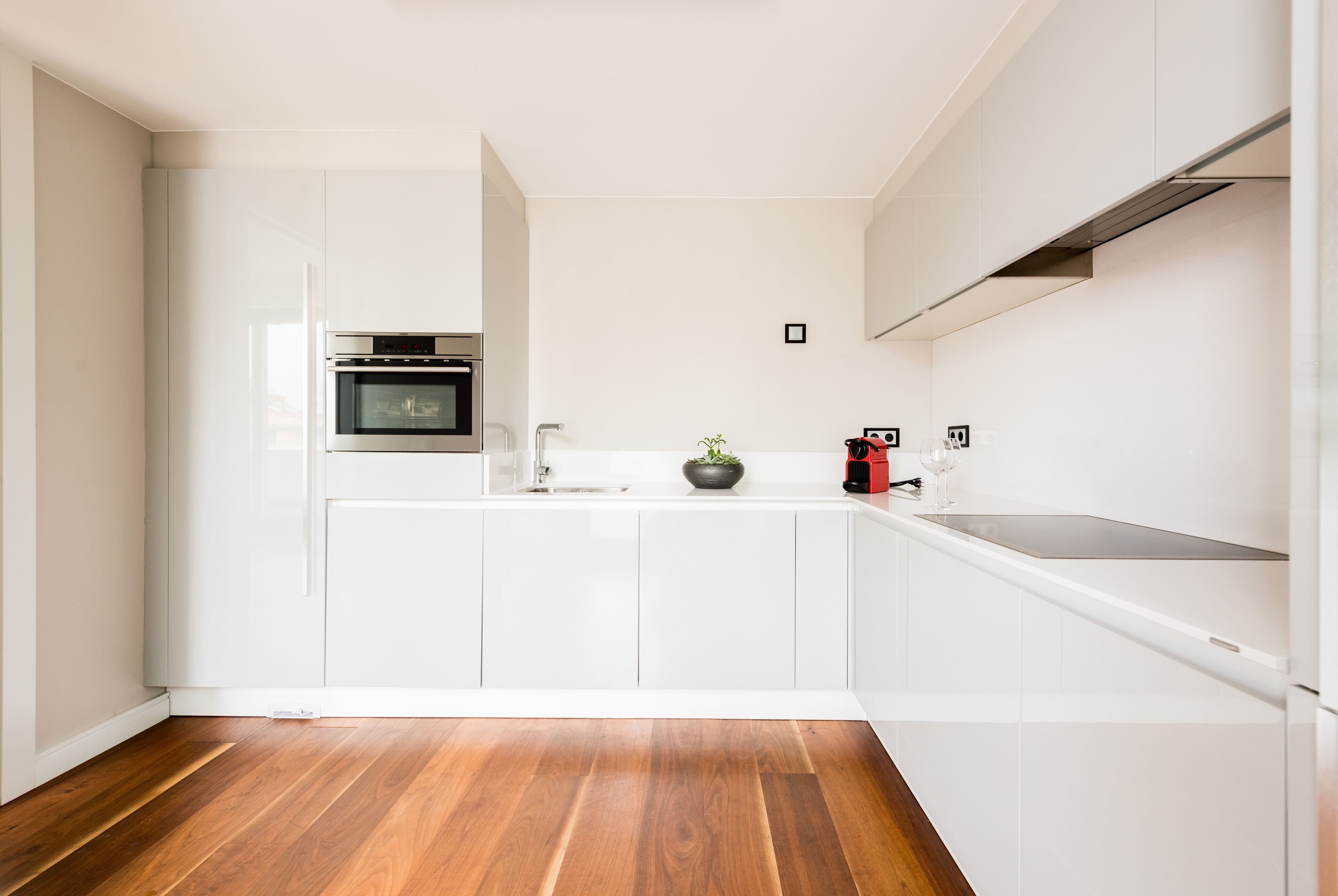A modern kitchen with white cabinetry, a wooden floor, and a built-in oven.