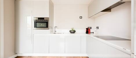 A modern kitchen with white cabinetry, a wooden floor, and a built-in oven.