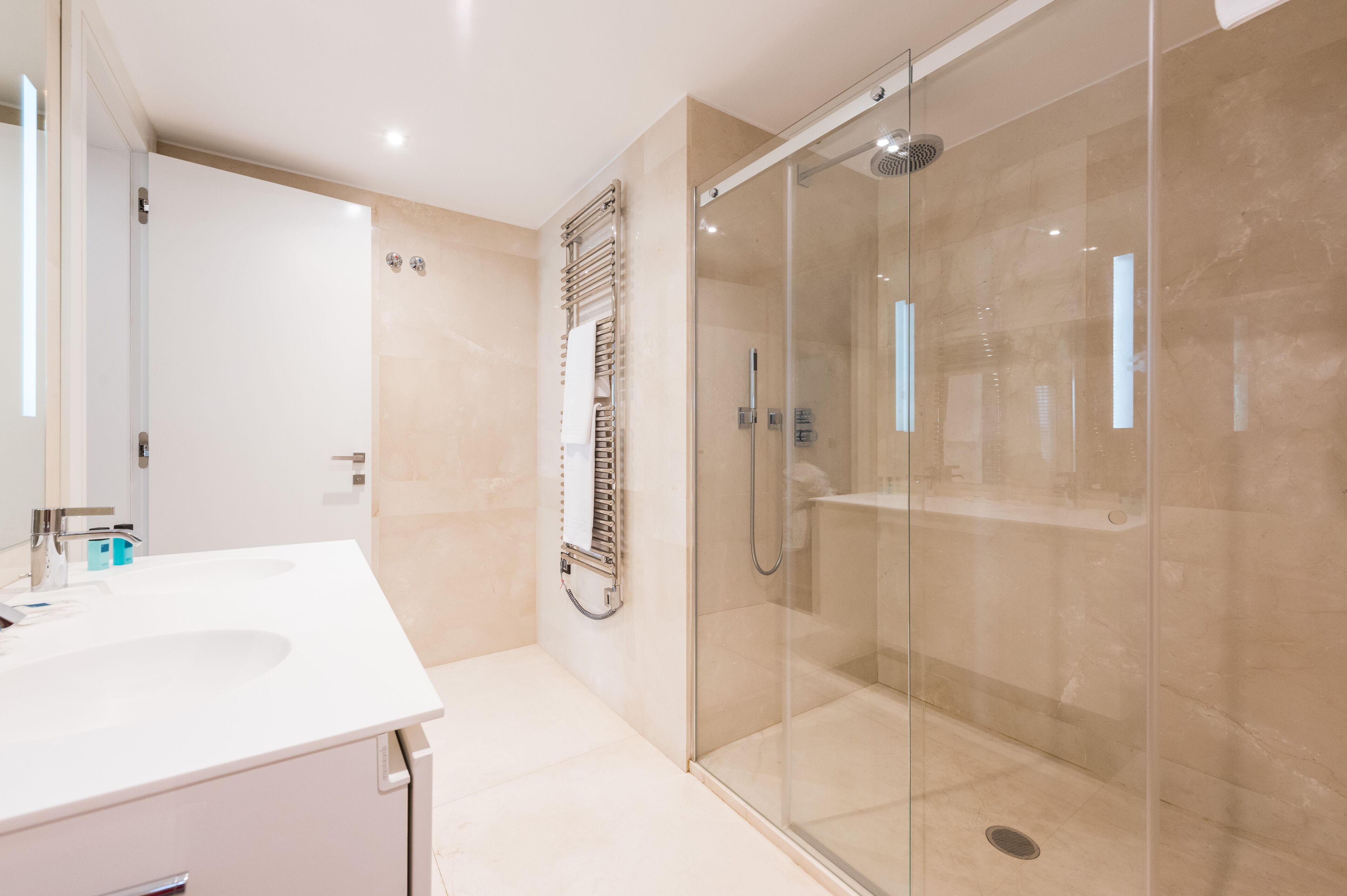 Un baño moderno con cabina de ducha de vidrio, un lavabo blanco y un perchero para toallas.