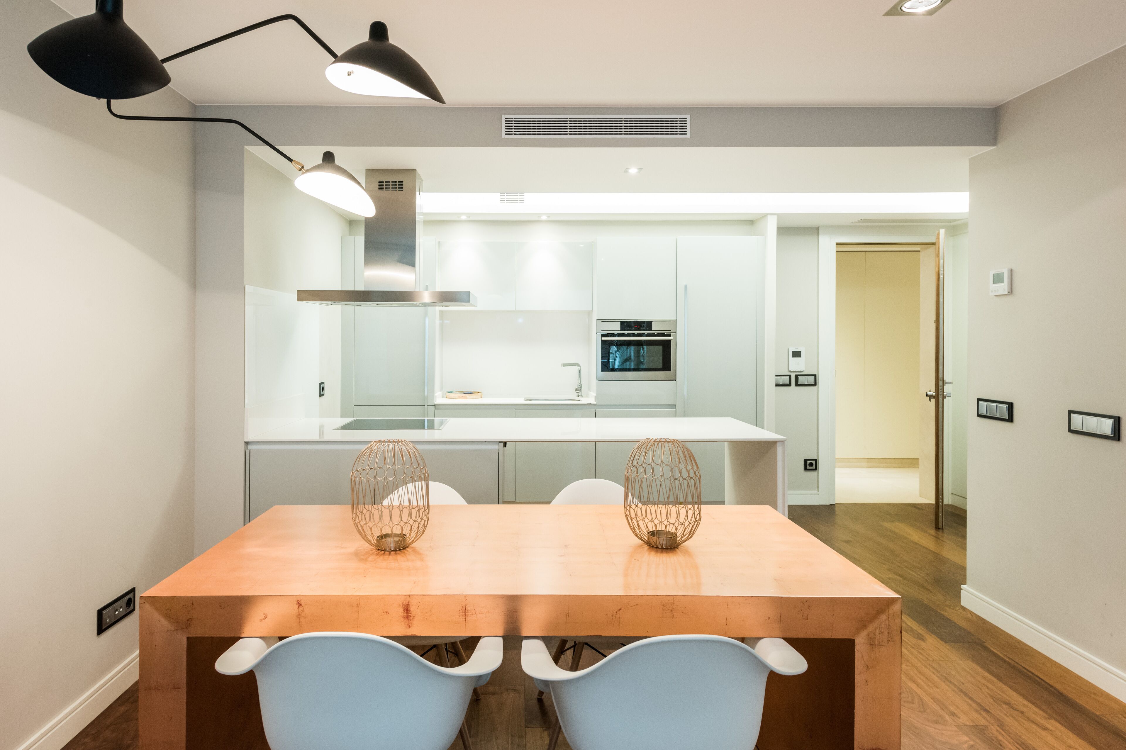 A modern kitchen with white cabinets, a built-in oven, and a dining area with a wooden table and two chairs.