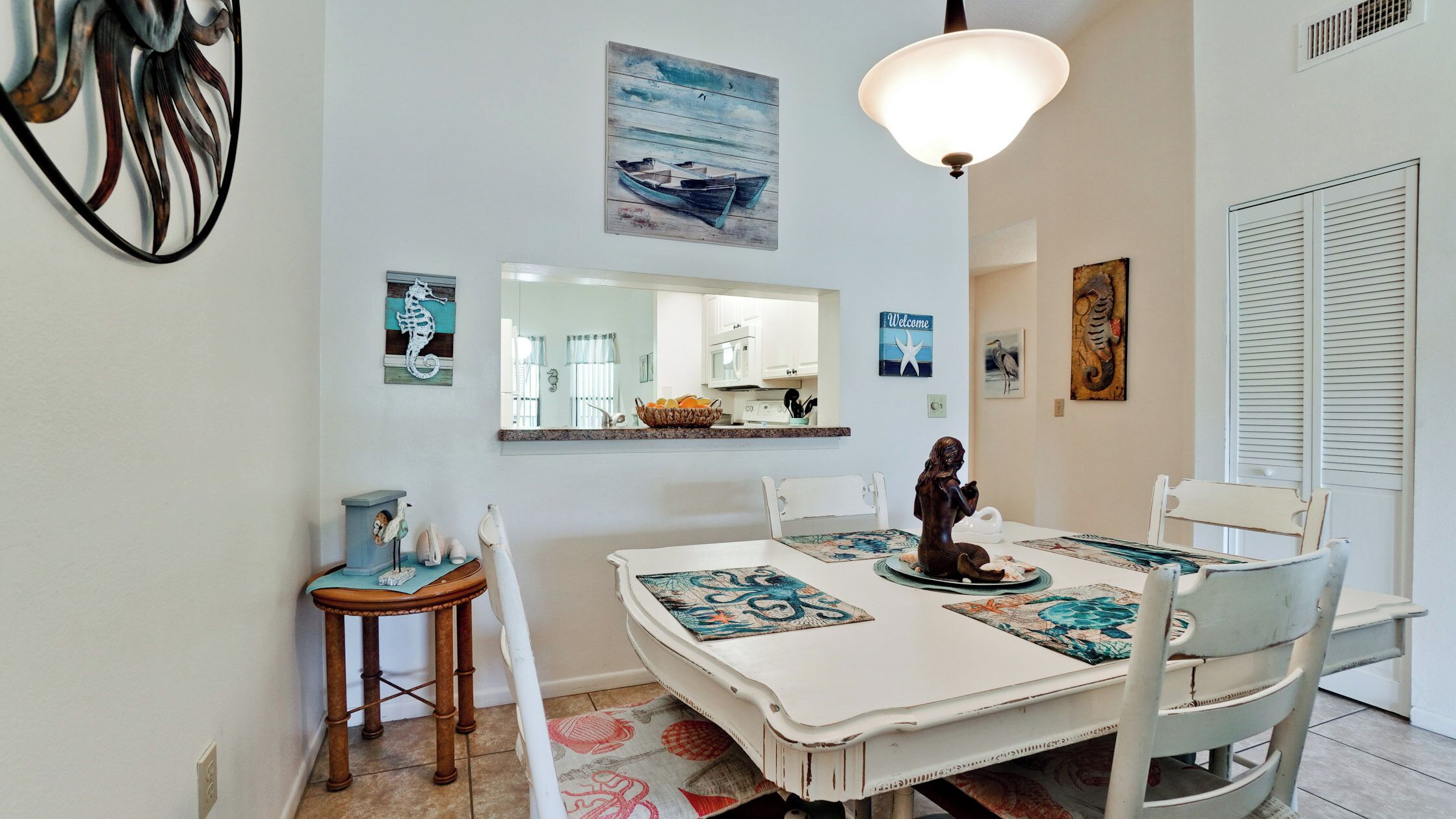 A dining area with a white table set for four, a decorative seahorse, and a 'Welcome' sign above the mirror.
