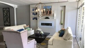 Un salon moderne avec un canapé blanc, un fauteuil blanc et une table basse. On y trouve une cheminée surmontée d’un élément décoratif.