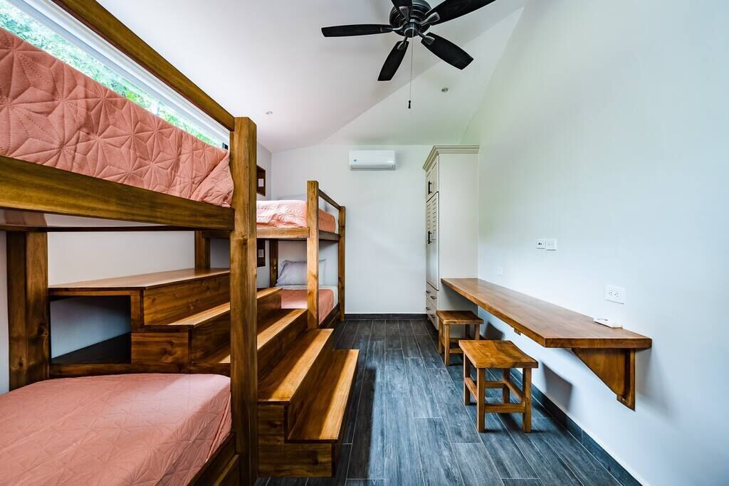 Quarto de dormitório com beliches, escrivaninha, cadeira e ventoinha no teto.