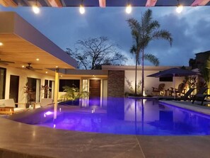 A modern outdoor pool area with a stone wall, palm trees, and lounge chairs. - Oasis del Mar★Private Pool w/ swim up bar and Walking Distance to TWO Beaches★ (Tamarindo)