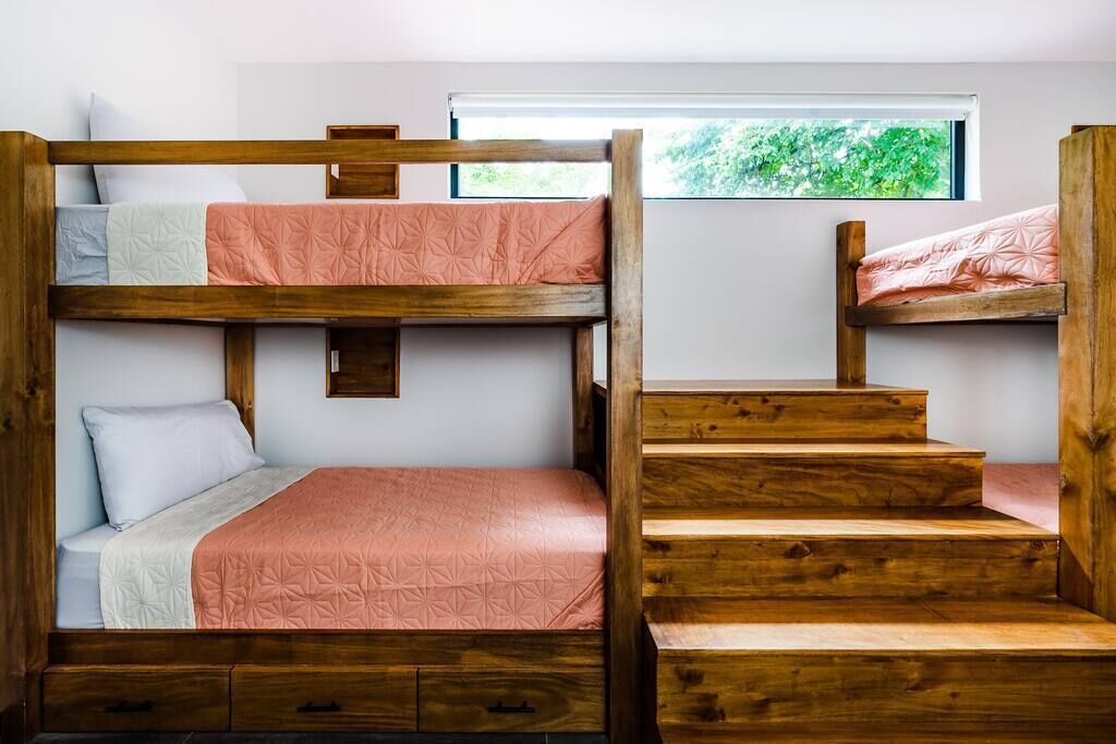 A bunk bed room with a window, wooden steps, and a small shelf.