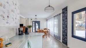 A modern kitchen with a dining area, featuring a coffee-themed wall, a large window, and a hanging light fixture.