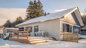 A snow-covered house with a wooden deck and a fenced yard.