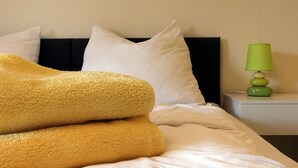 Een opgemaakt bed met witte lakens en een geel dekbed, een groene lamp op een nachtkastje, en witte kussens.