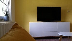 Een moderne woonkamer met een witte televisiemeubel, een flatscreen televisie, een klein rond tafeltje en een gele wand.