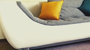 Een moderne woonkamer met een grijze bank, twee ronde houten tafels en kleurrijke kussens.