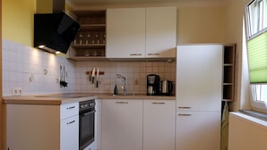 Een moderne keuken met witte kastjes, een inbouwoven, een koffiezetapparaat en een raam met jaloezieën.