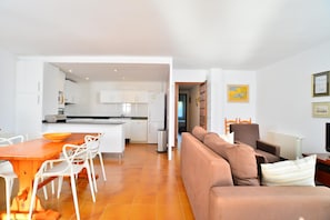 A modern living room with a brown sofa, a dining table with chairs, and a kitchen in the background.