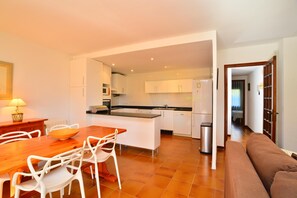 A modern kitchen with white cabinets, a dining area with a wooden table and white chairs, and a brown sofa in the living area.
