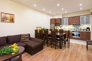 Uma cozinha moderna com armários de madeira, uma sala de jantar com mesa e cadeiras, e uma sala de estar com sofá e planta.