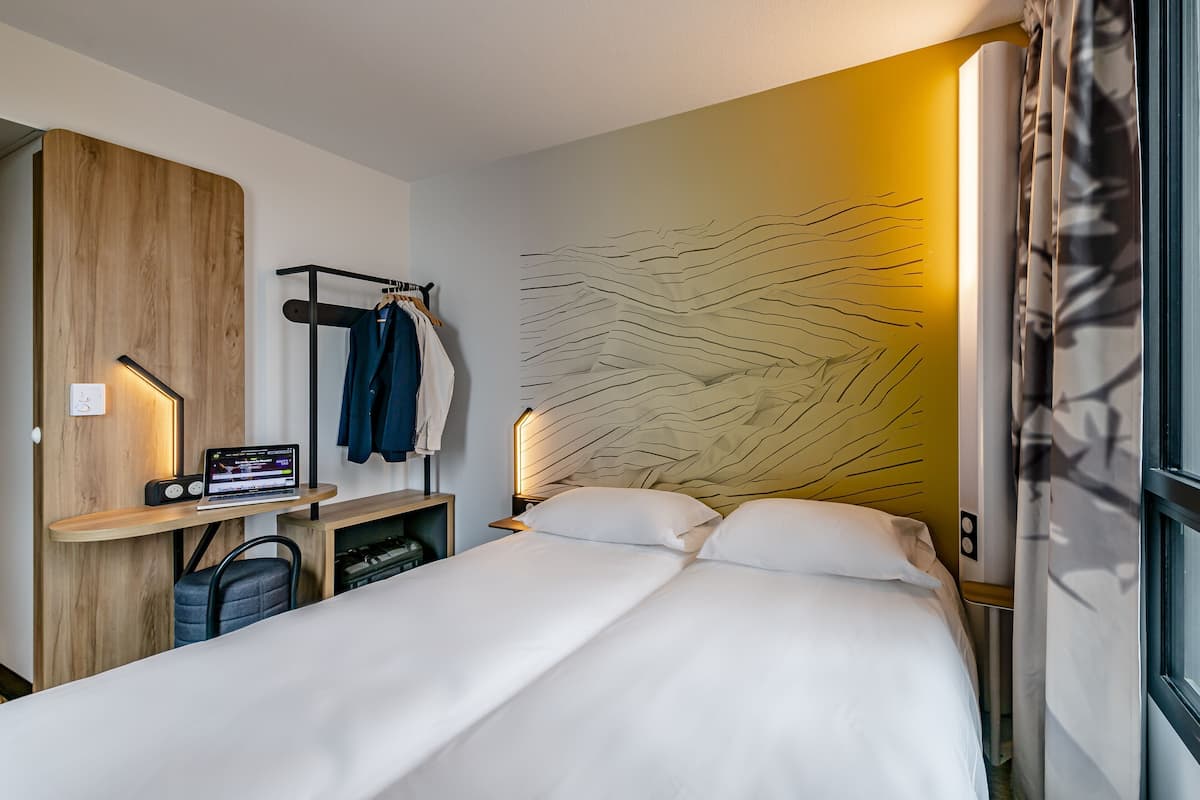 Habitació d'hotel amb un llit, un escriptori amb un ordinador portàtil, una perxa per a abrics i una paret amb un disseny amb relleu.