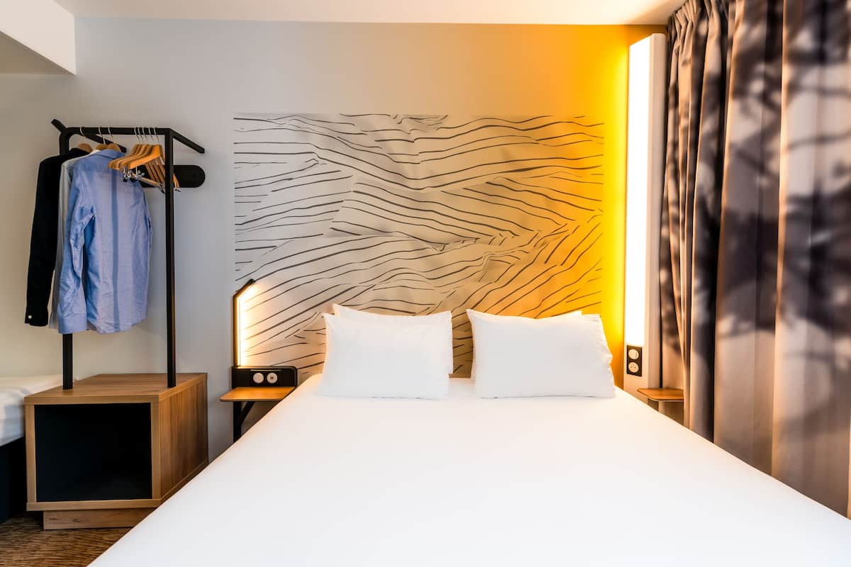 Habitació d'hotel moderna amb un llit gran, una taula de nit amb una làmpada, un armari i una paret amb un disseny texturat únic.