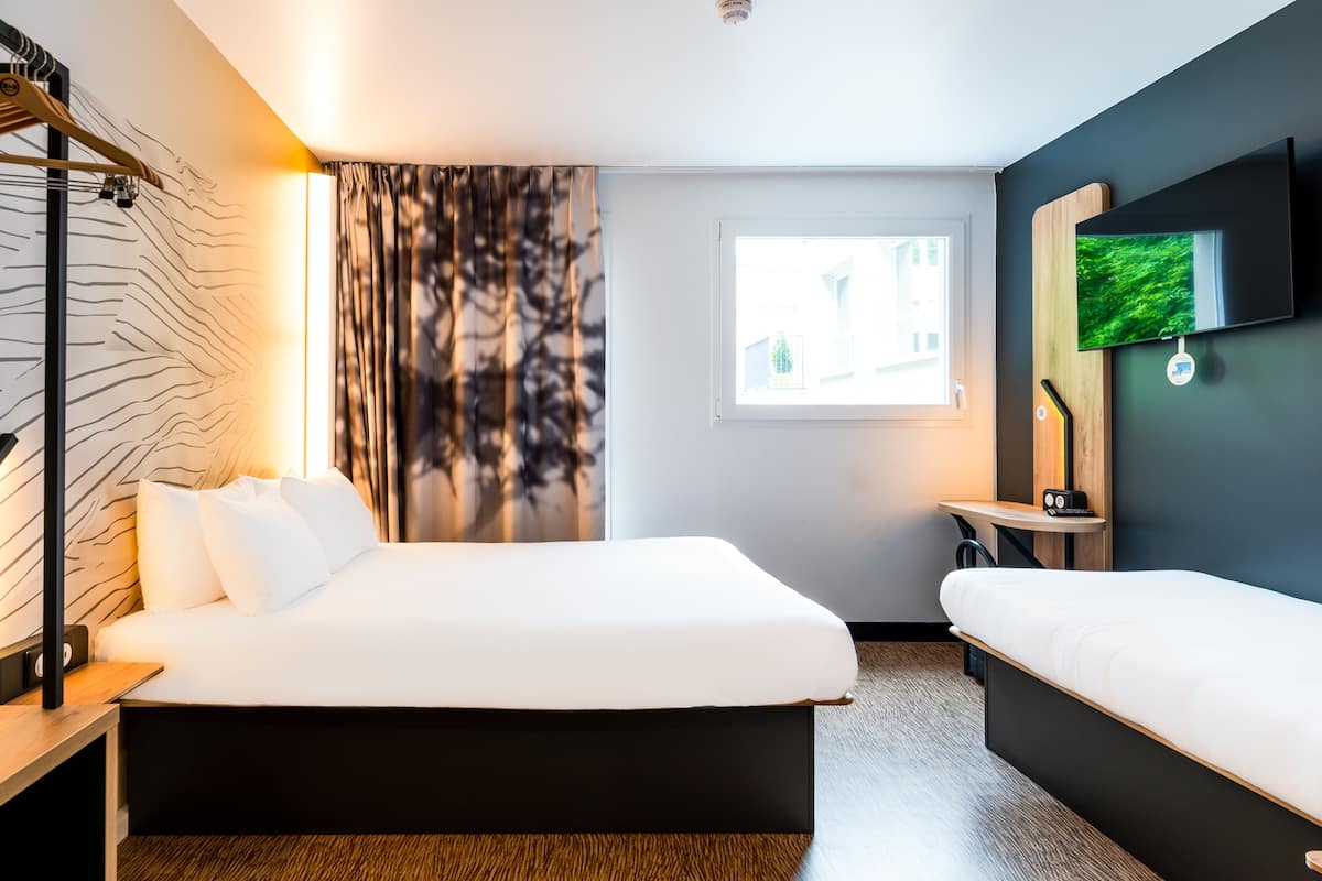 Habitació d'hotel moderna amb un llit gran, una taula de nit, un televisor fixat a la paret i una finestra amb vista a edificis.