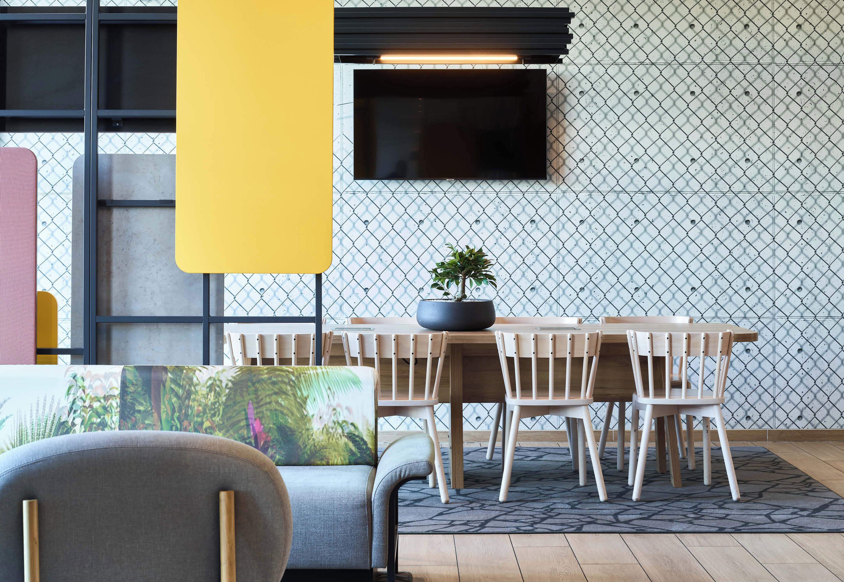 A dining area with a table and chairs, a potted plant, and a television mounted on a patterned wall.