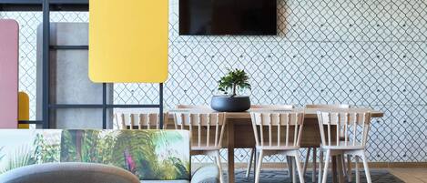 A dining area with a table and chairs, a potted plant, and a television mounted on a patterned wall.
