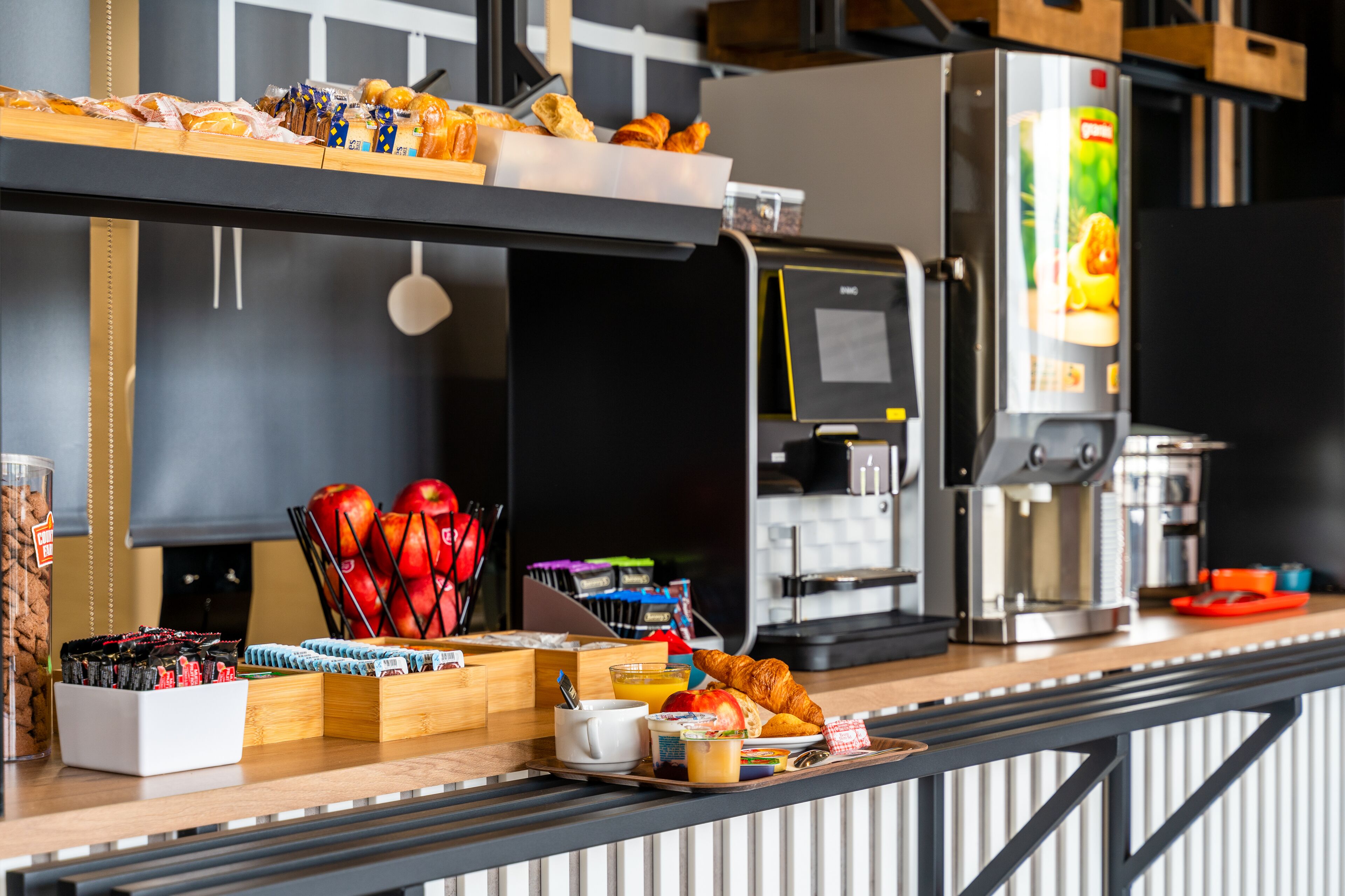 A breakfast bar with pastries, fruits, and a coffee machine.