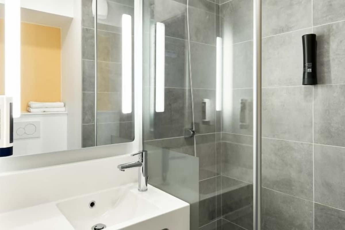 Ein modernes Badezimmer mit einem weißen Waschbecken, einem großen Spiegel und einer Duschkabine aus Glas.