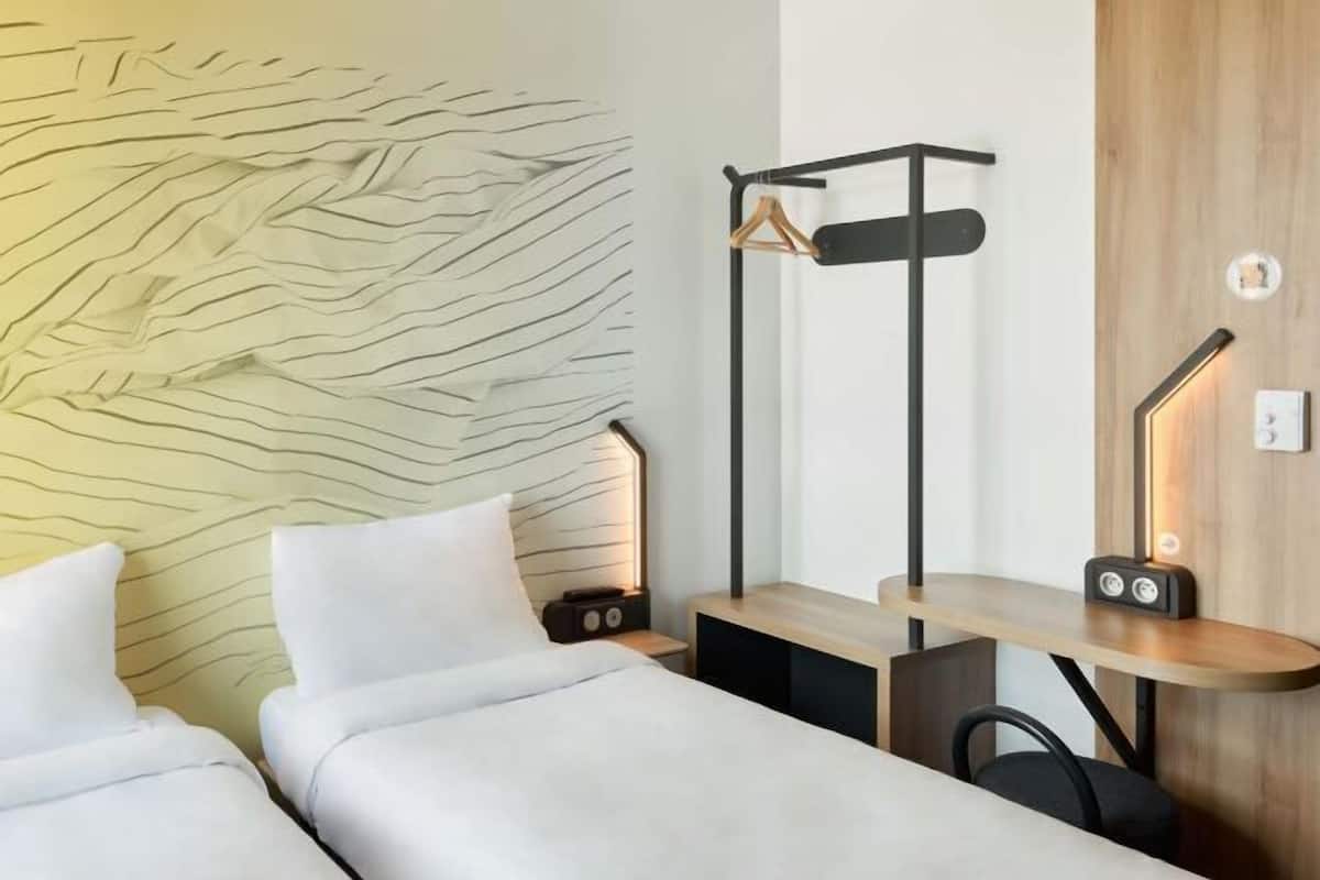 A hotel room with a bed, bedside tables, a wall-mounted hanger, and a desk with a chair.