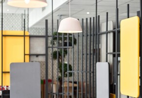 Un interior moderno con una lámpara colgante, separadores metálicos y una planta de fondo.