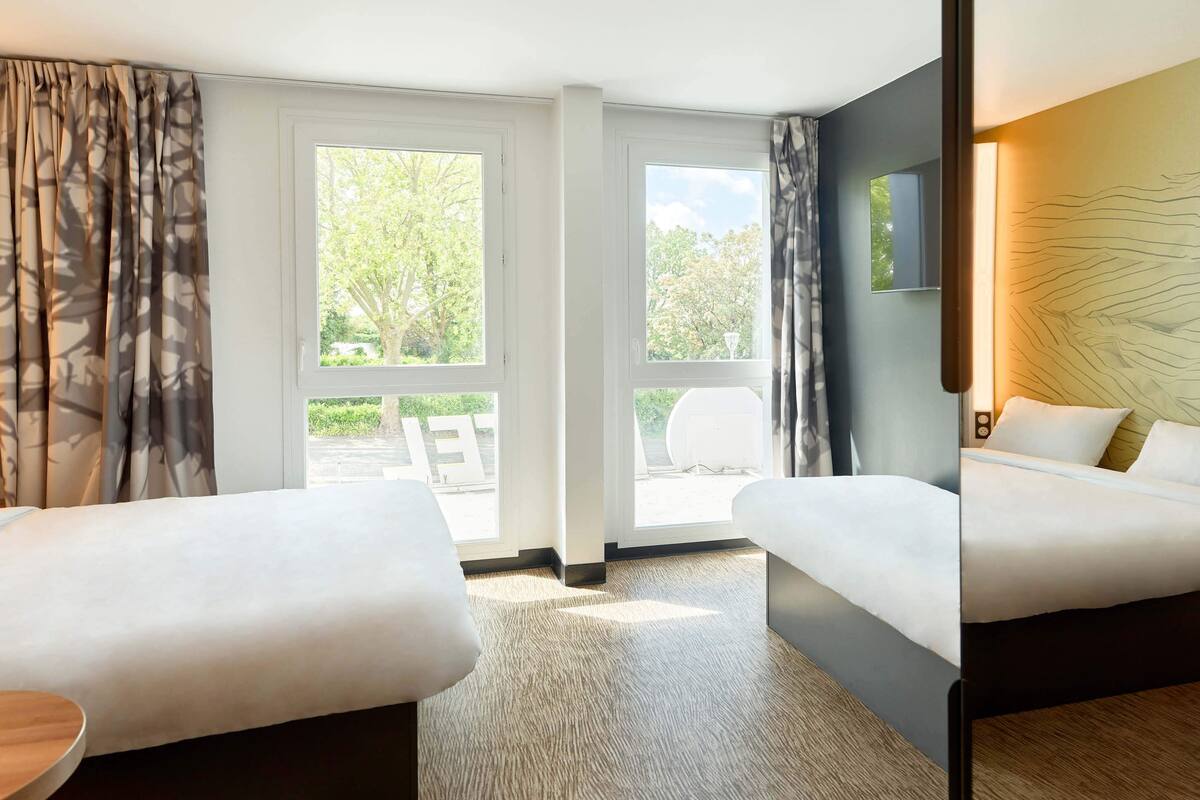 A hotel room with two beds, a large window with a view of greenery, and a modern design.