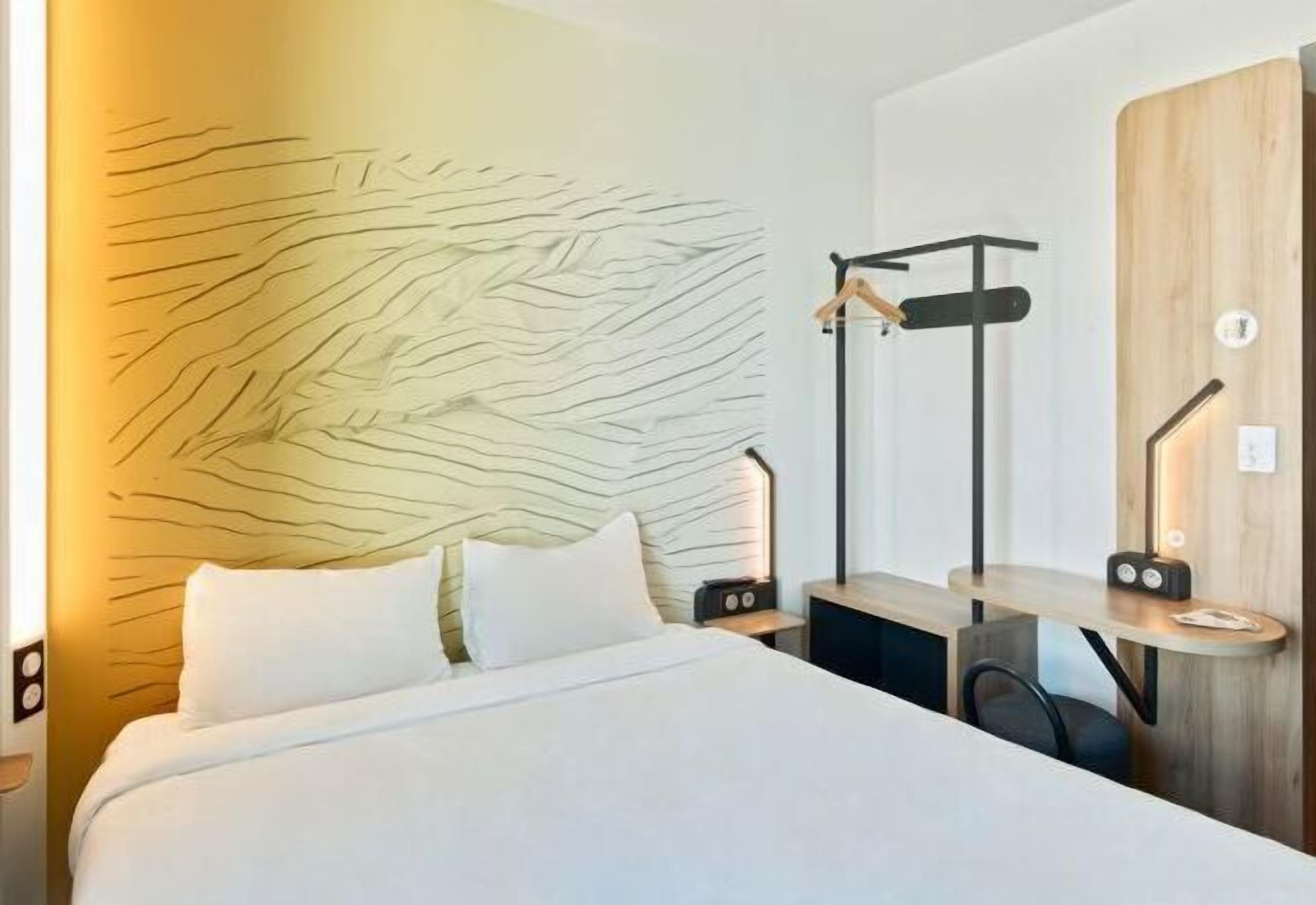 Ein modernes Hotelzimmer mit Bett, Nachttischen, einem Holz-Kopfteil und einem an der Wand befestigten Kleiderhaken.