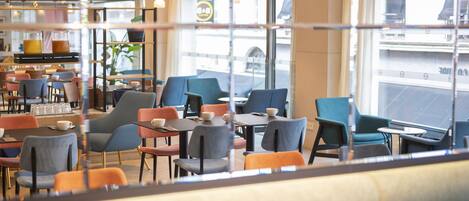 A modern cafe with multiple seating areas, including tables and chairs, and large windows offering a view of the street.
