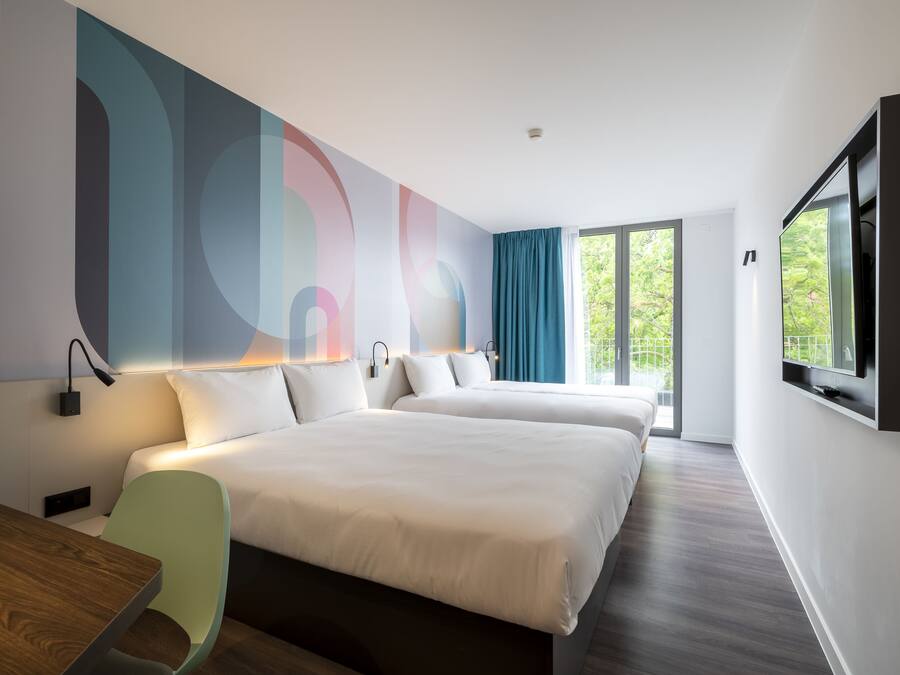 Une chambre d’hôtel moderne avec deux lits, une télévision et une grande fenêtre avec des rideaux.