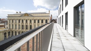 Un balcón con vista a un edificio clásico con ventanas arqueadas y un elemento decorativo central.
