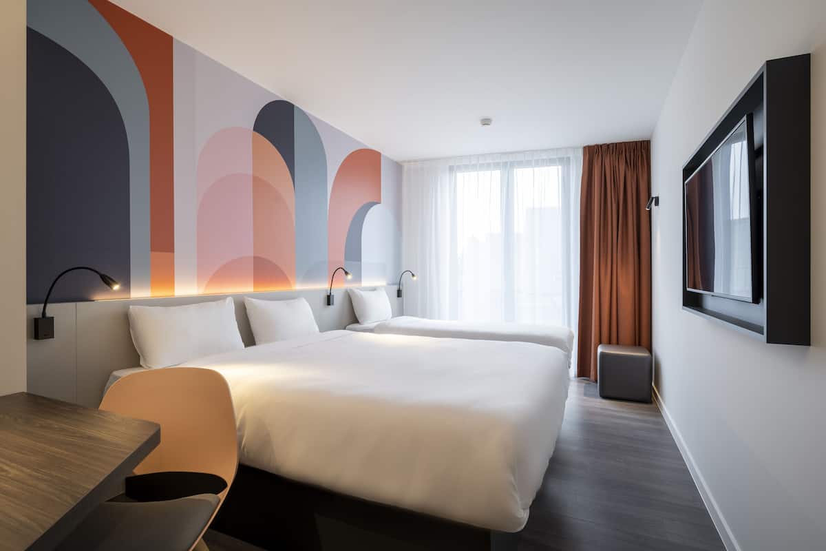 A modern hotel room with a large bed, a desk, and a TV mounted on the wall.