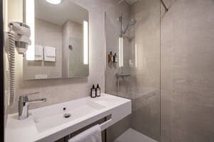 Un baño moderno con un lavabo blanco, un secador de pelo y una ducha con cerramientos de vidrio.