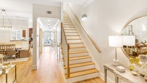 A spacious hallway with a wooden staircase leading to a dining area. - Chic Townhome One Block From Forsyth w/ Large Garage by Lucky Savannah (Savannah)