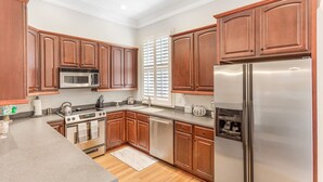 A modern kitchen with wooden cabinets, stainless steel appliances, and a large window with blinds. - Chic Townhome One Block From Forsyth w/ Large Garage by Lucky Savannah (Savannah)