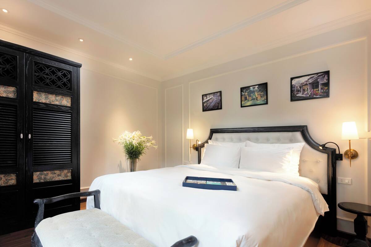 A neatly made bed with a blue tray, a white upholstered chair, and a black wardrobe with decorative panels.