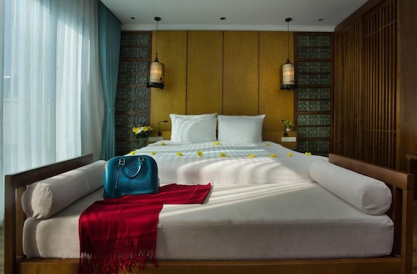 A hotel room with a bed, a red throw blanket, a blue bag, and two wall-mounted lamps.