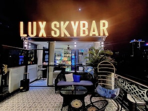 A rooftop bar named 'LUX SKYBAR' with a bar area, seating, and a view of the cityscape.