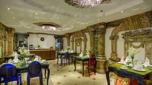 A restaurant with ornate stone columns, a chandelier, and tables set for dining.