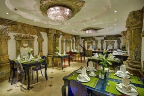 A dining area with ornate columns, chandeliers, and a marble floor. Tables are set with white tableware and green placemats. - Hanoi Media Hotel And Spa (Hanoi)