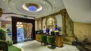 A lobby with a reception desk, green chairs, a chandelier, and a stone wall with columns.