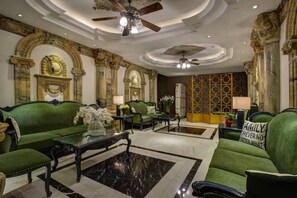 A luxurious lobby with green upholstered sofas, marble flooring, ornate wall decorations, and ceiling fans. - Hanoi Media Hotel And Spa (Hanoi)
