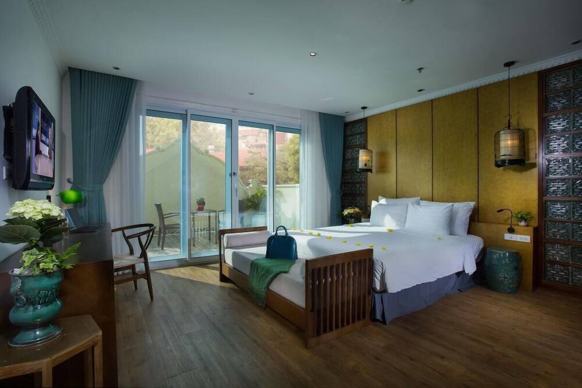 A bedroom with a bed, a desk, a chair, a large window, and a view of greenery.