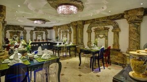 A dining area with tables set for service, ornate columns, and a chandelier.
